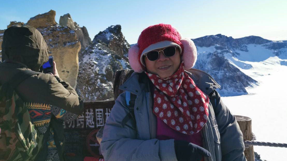Jean wearing winter clothes, standing in front of a snowy mountain scenery.